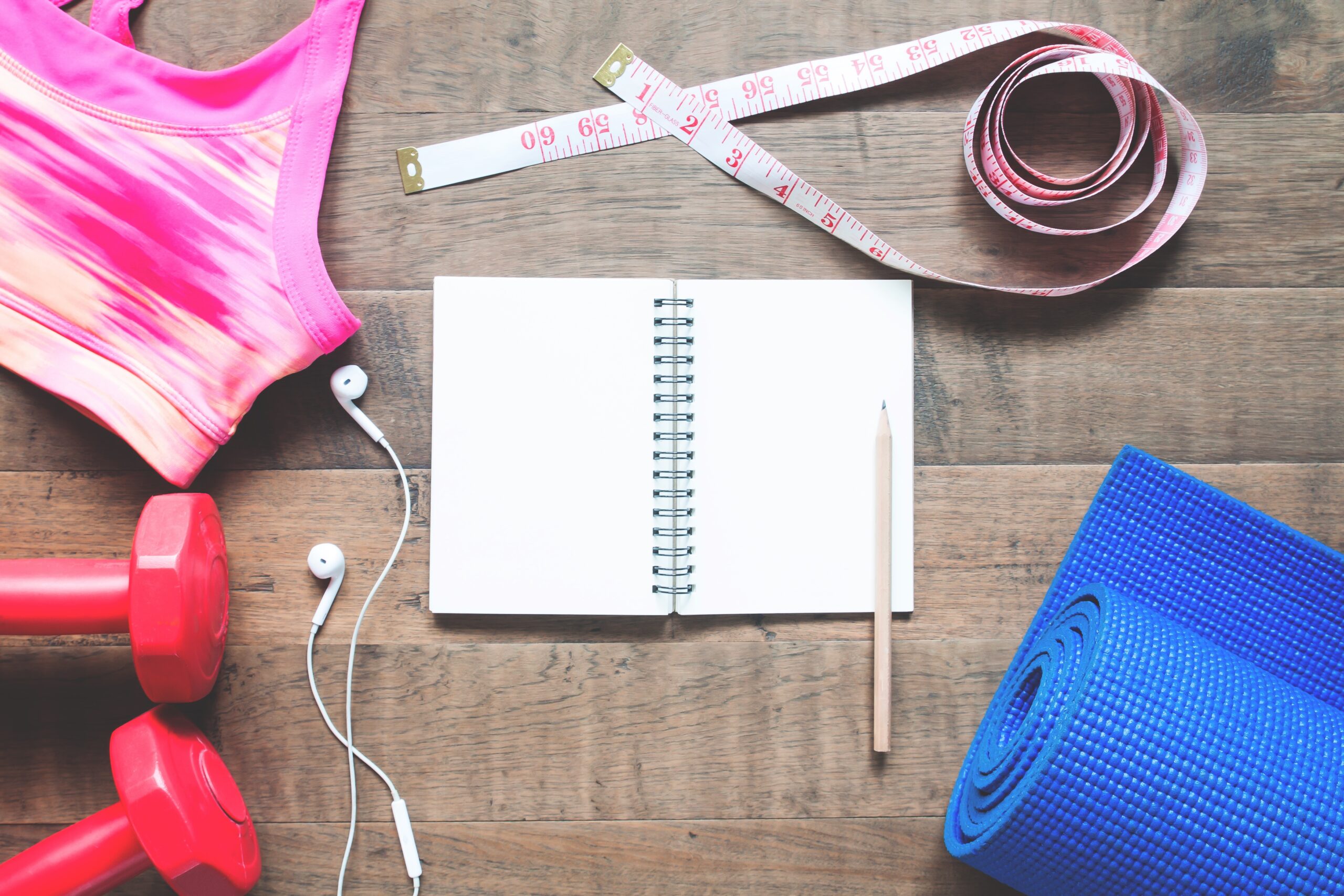 Creative flat lay of blank notebook with sport equipments on wooden floor